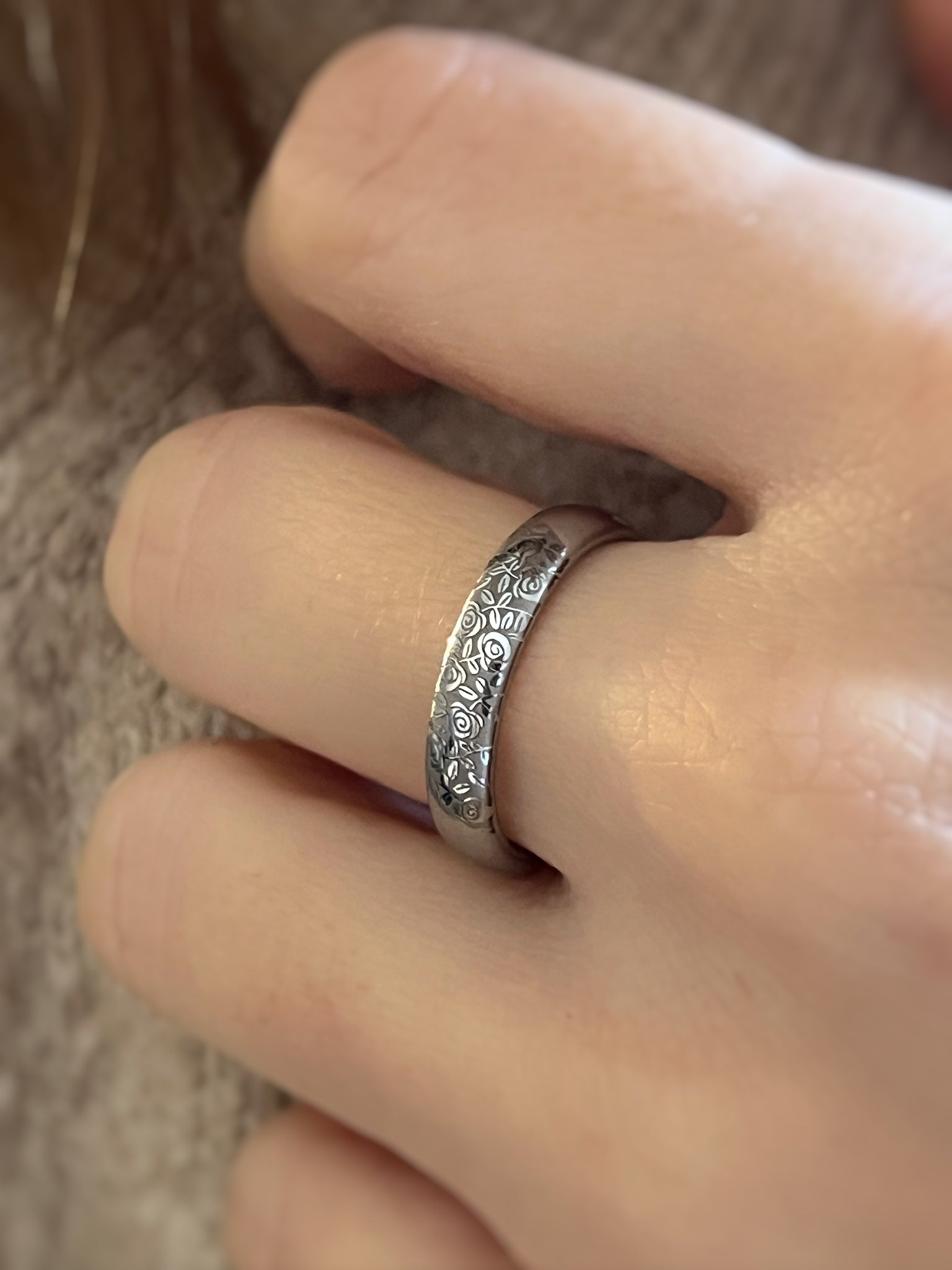 Silver ring with floral intricate design on a finger against a blurred background