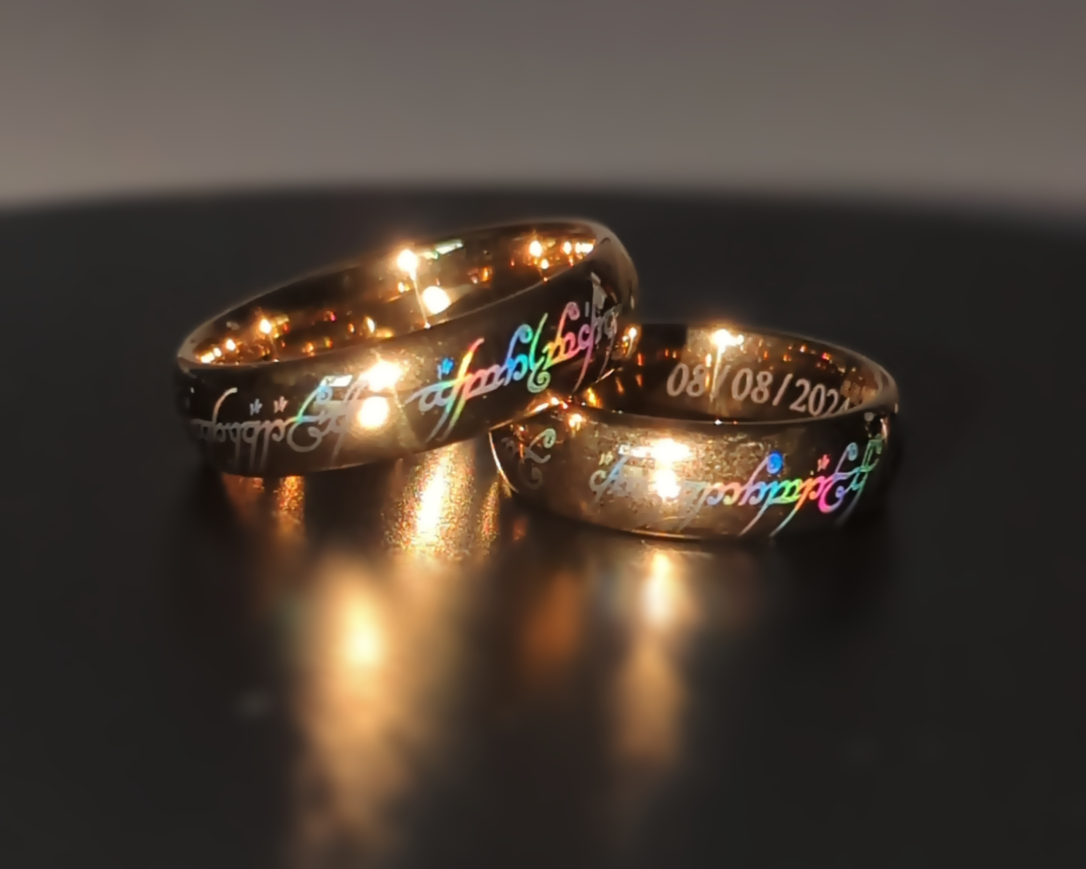 Two gold rings with engraved text on a reflective surface
