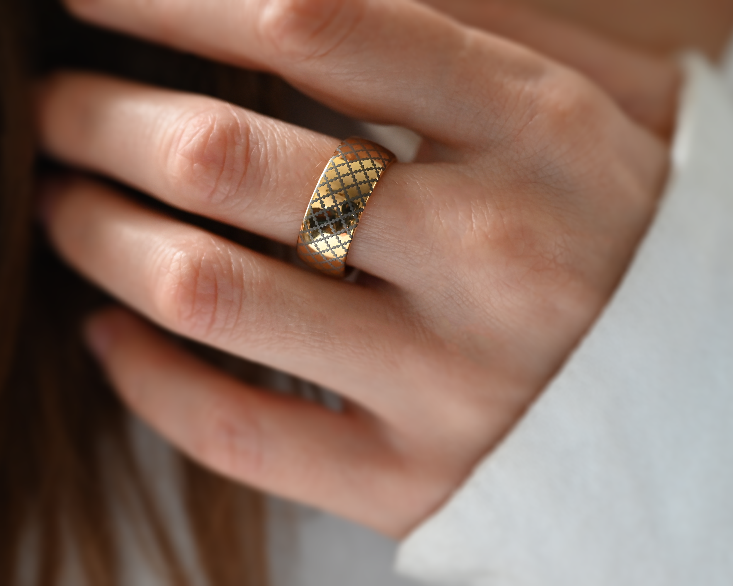 Close-up of a hand wearing a gold tungsten carbide ring with a delicate silver-grey engraved geometric pattern, elegant unisex design, durable and scratch-resistant jewelry photographed in soft natural light.