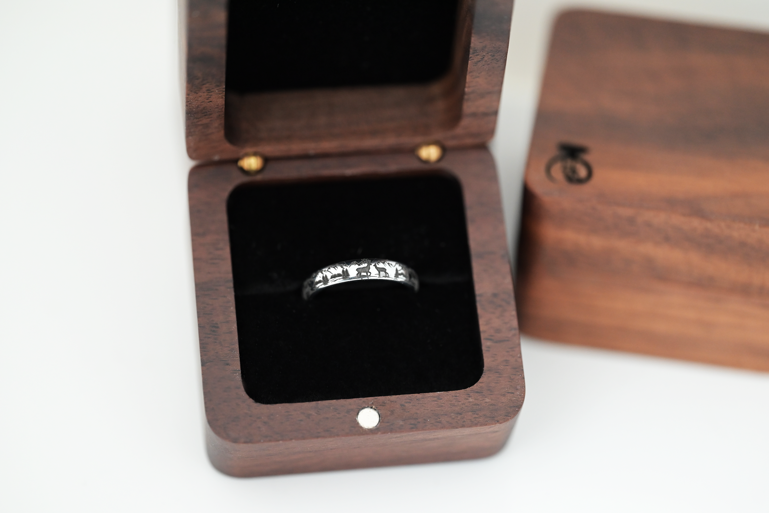Nature inspired tungsten ring with detailed laser engraving of mountains and deer. Ring is placed inside a wooden box.