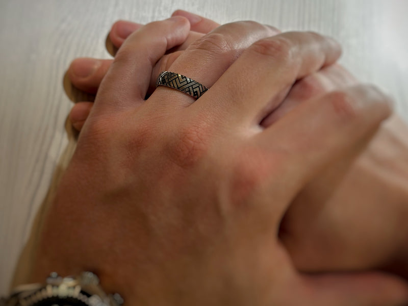 The Labyrinthine Loop tungsten ring with laser-engraved surface detail, worn on a hand.