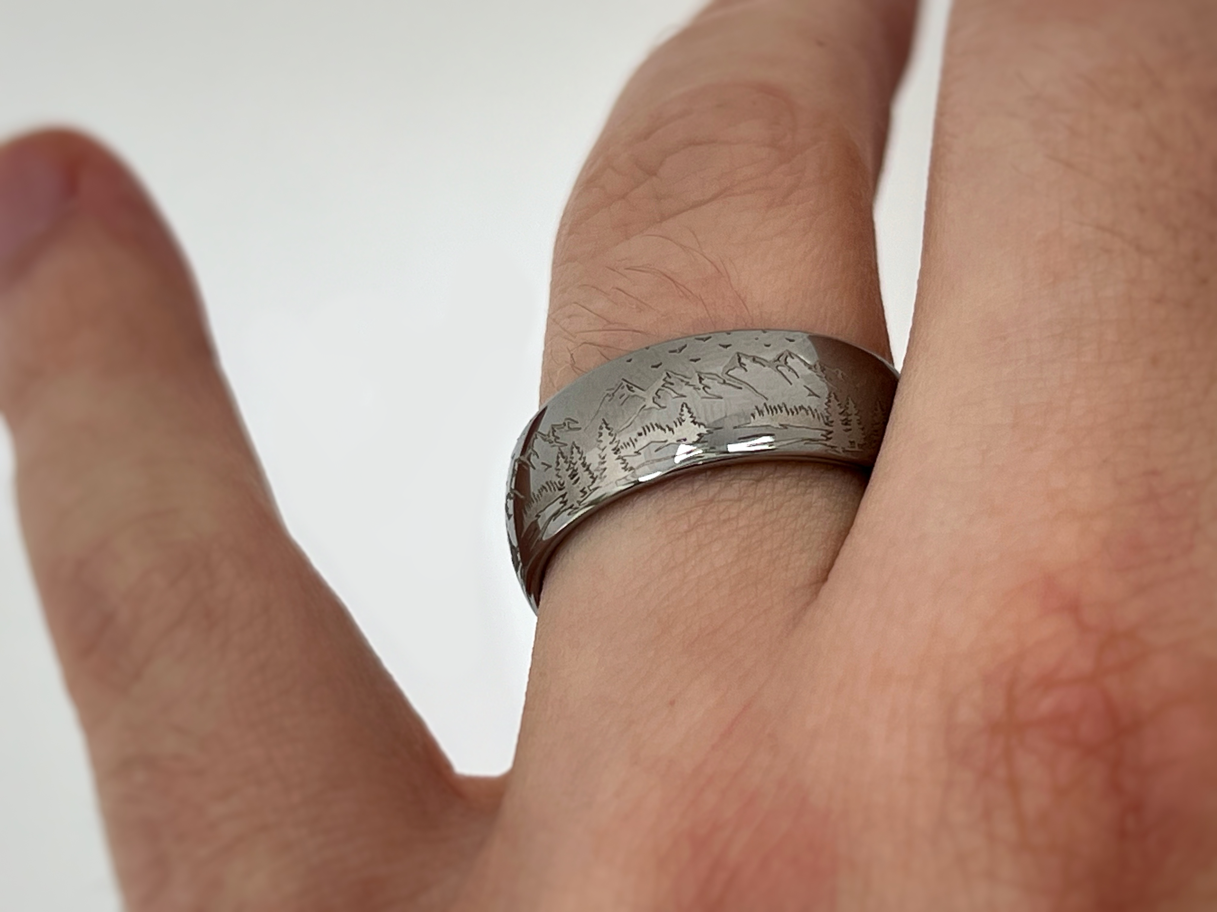 Silver tungsten ring with an engraved mountain range design, isolated on a white background.