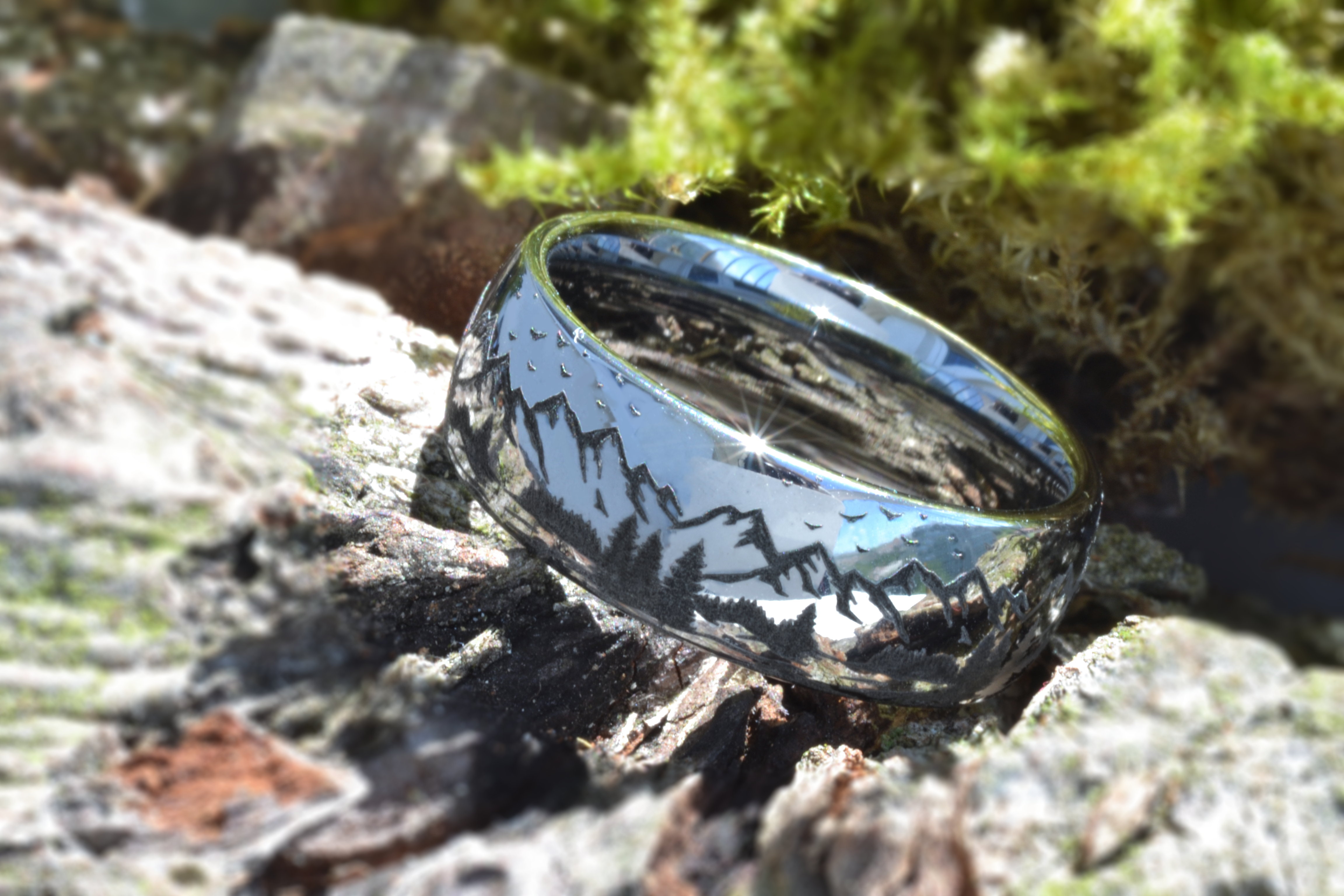 Silver tungsten ring with an engraved mountain range design, placed on a piece of bark with moss, showcasing the nature-inspired engraving.