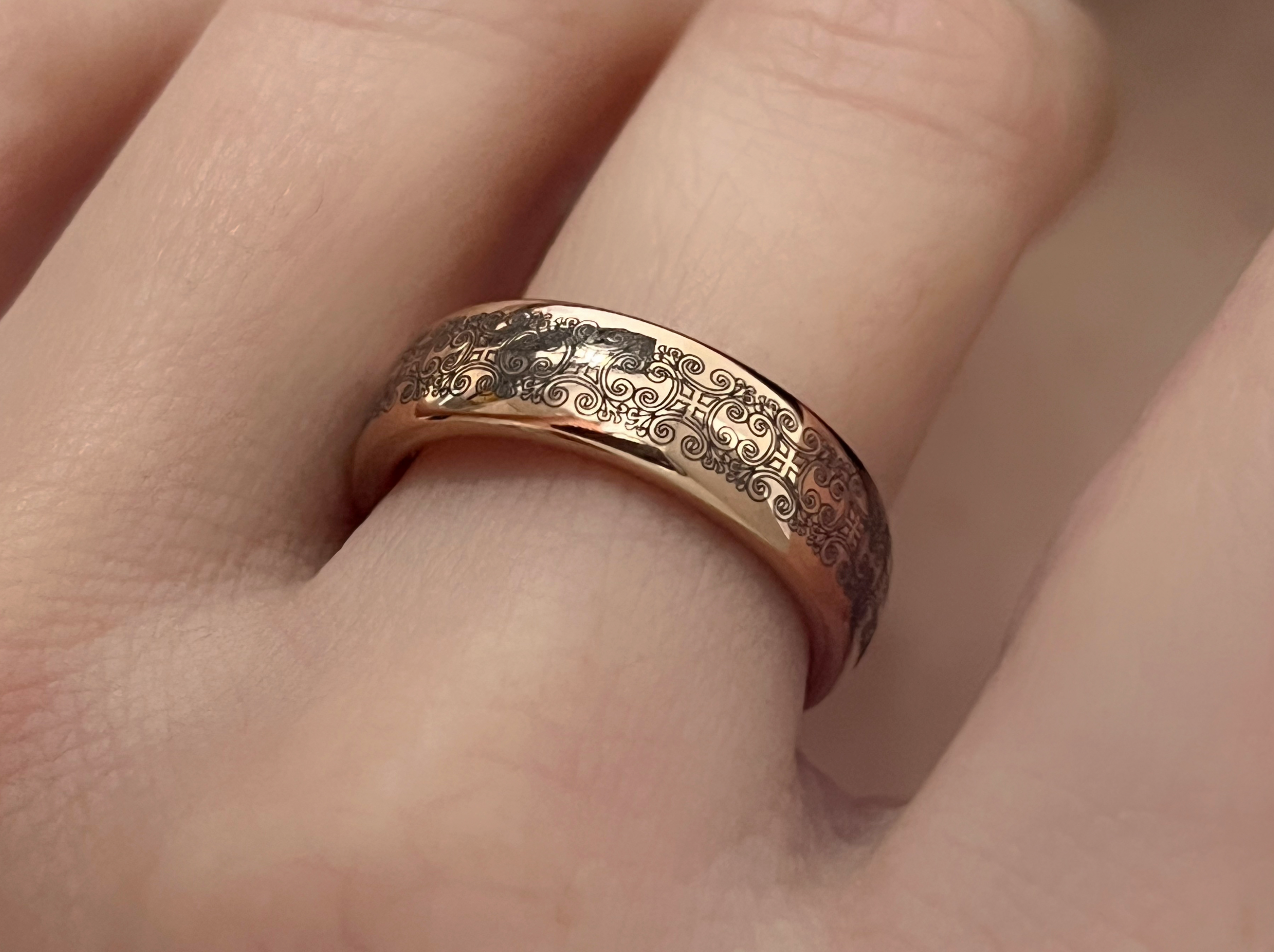 Close-up of a rose-gold tungsten ring with detailed antique-style engravings worn on a finger, showcasing its intricate design and rose gold interior.