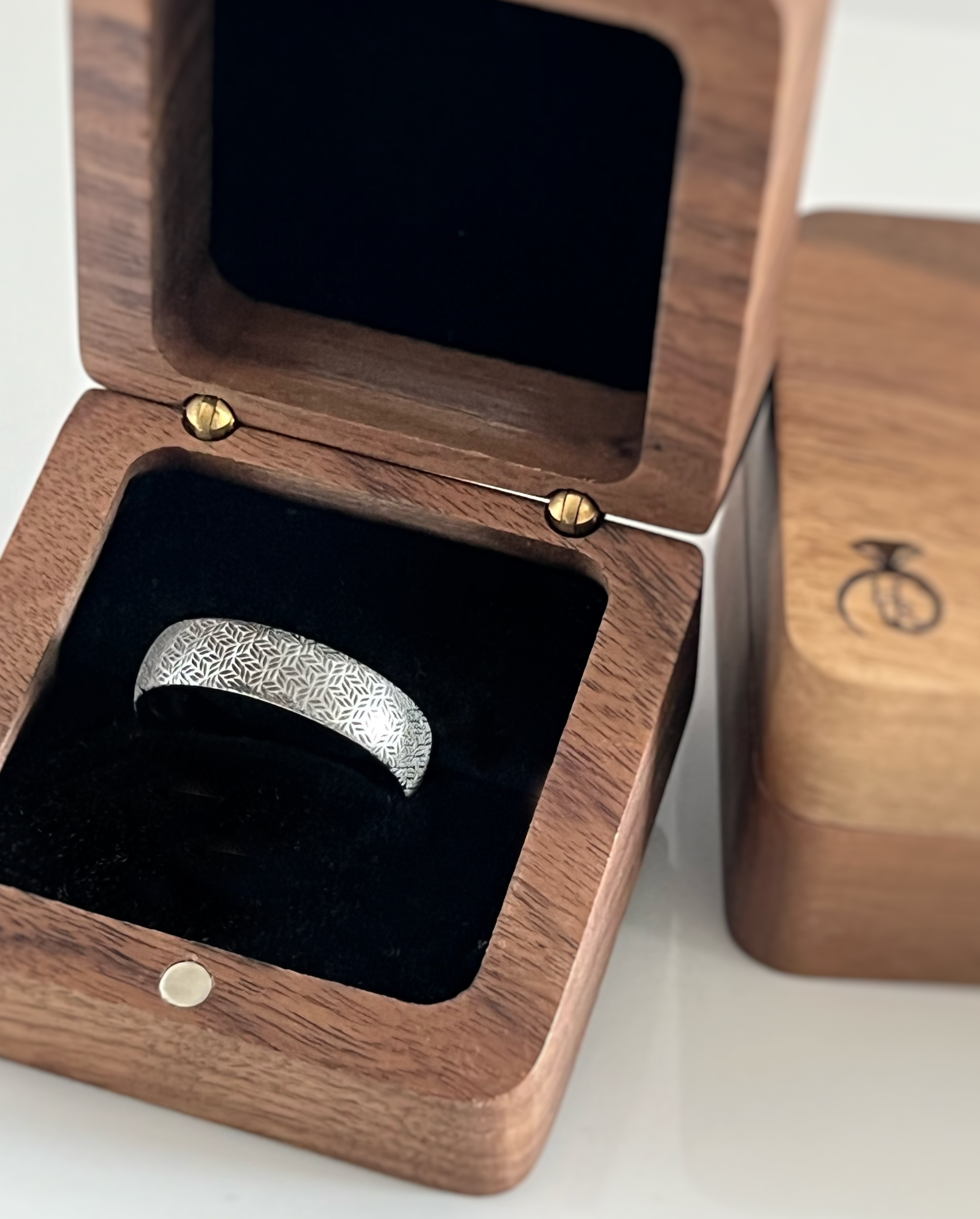 Silver tungsten ring with an intricate leaf pattern, displayed in an open wooden ring box with a black interior.