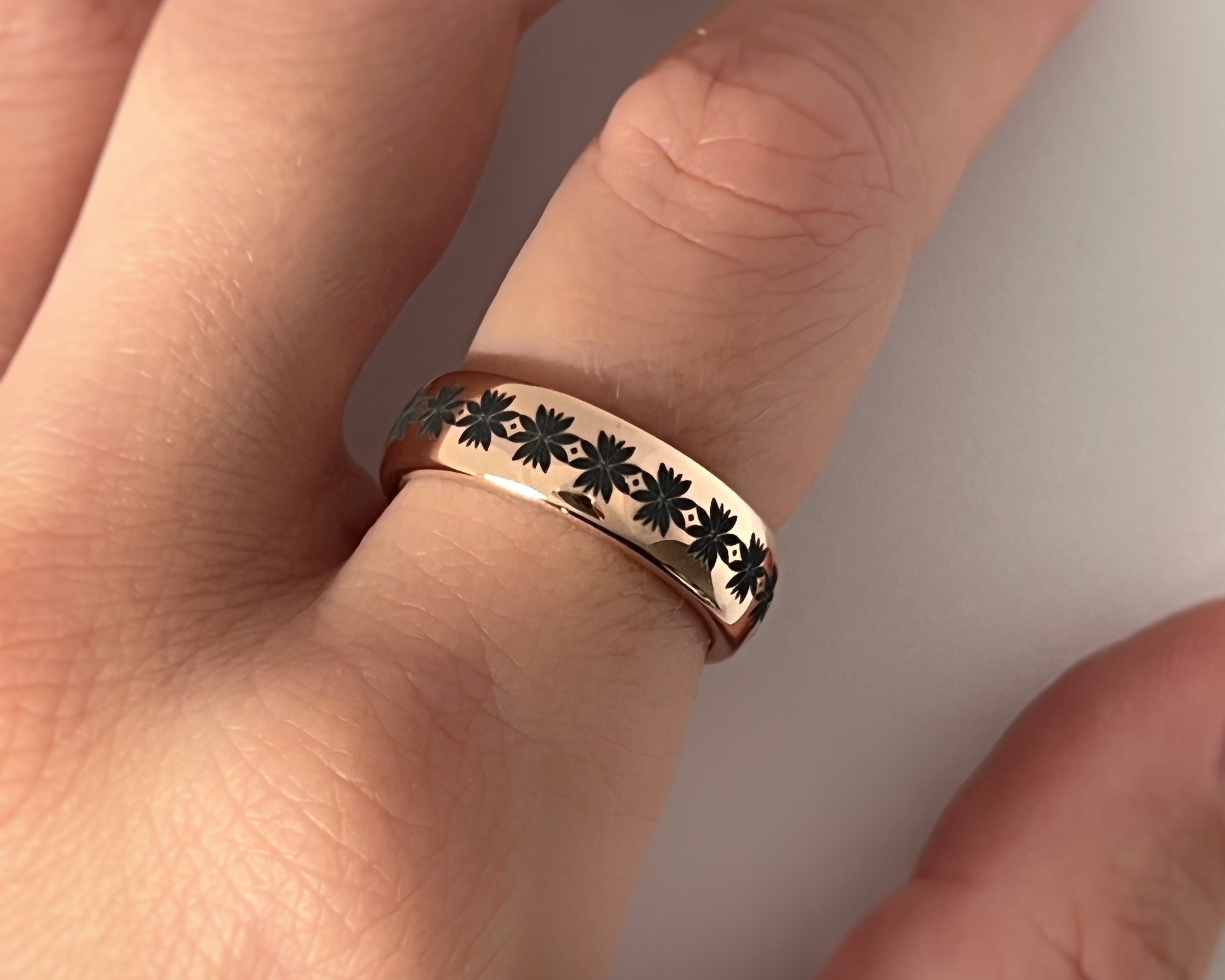 Gold ring with black floral design on a hand against a white background