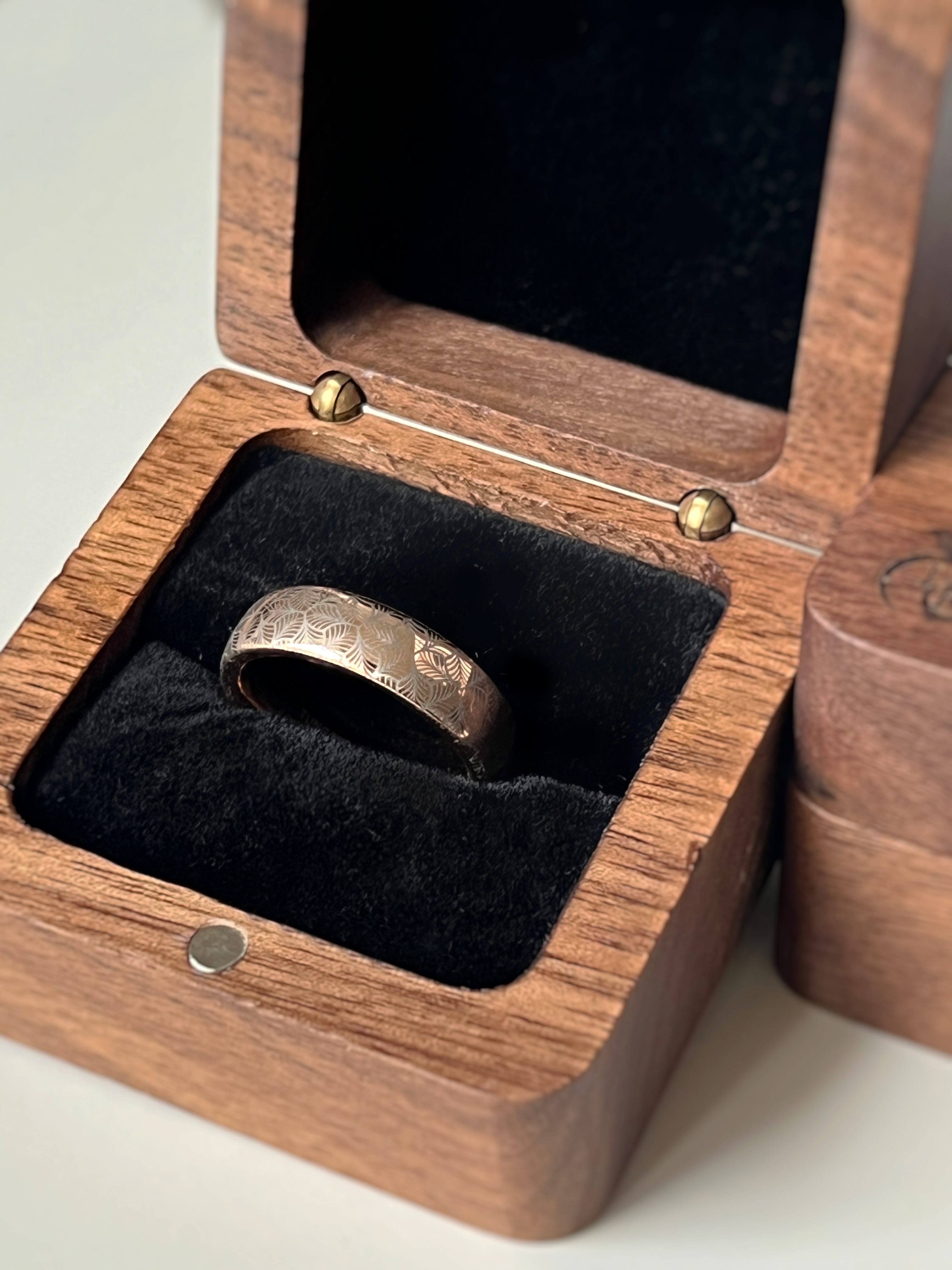 Rose gold tungsten ring with an intricate, white-engraved petal-like pattern, inside wooden box offering a delicate and refined look, perfect for weddings, special occasions, or everyday wear.