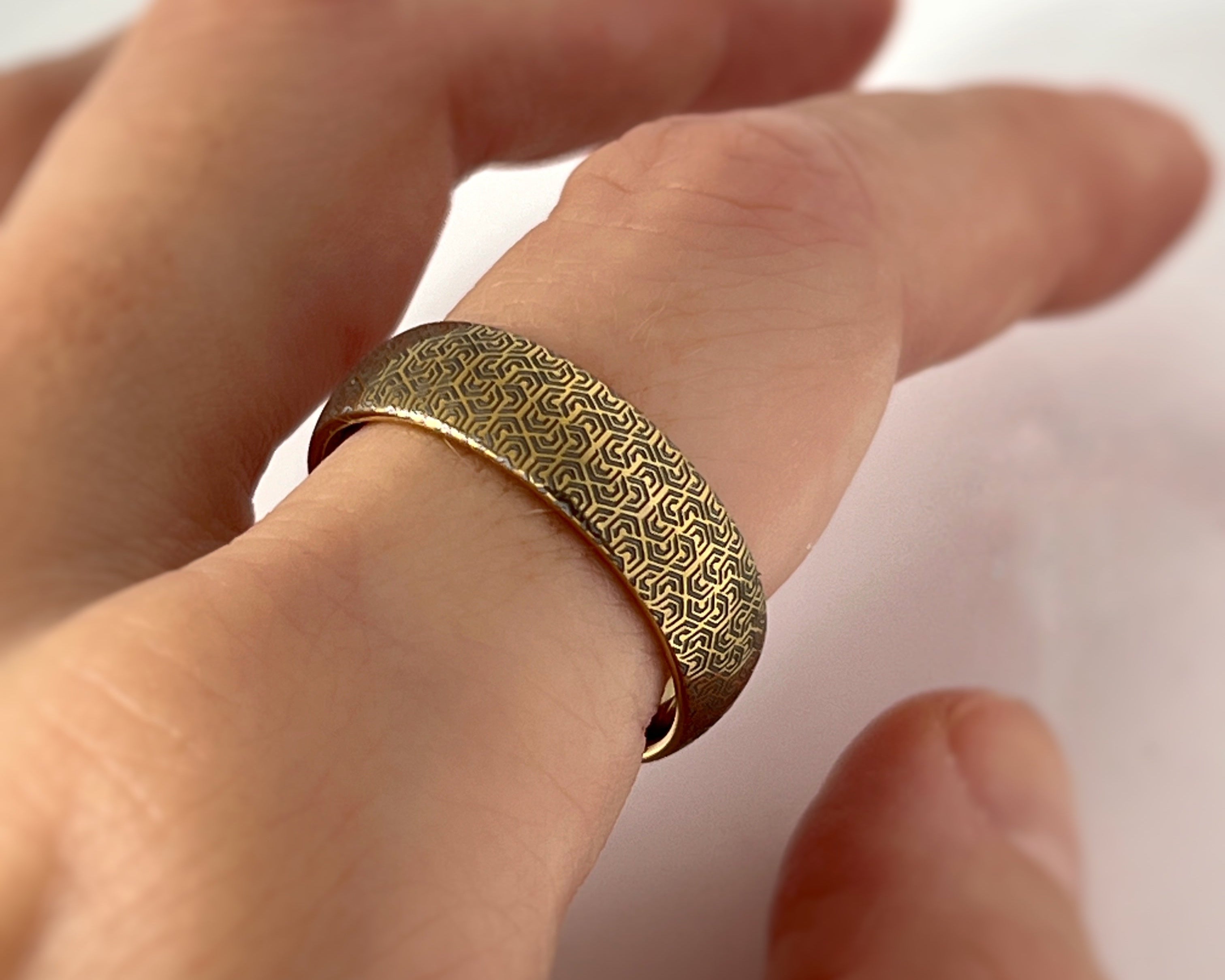 Gold ring with intricate pattern worn on a finger against a white background