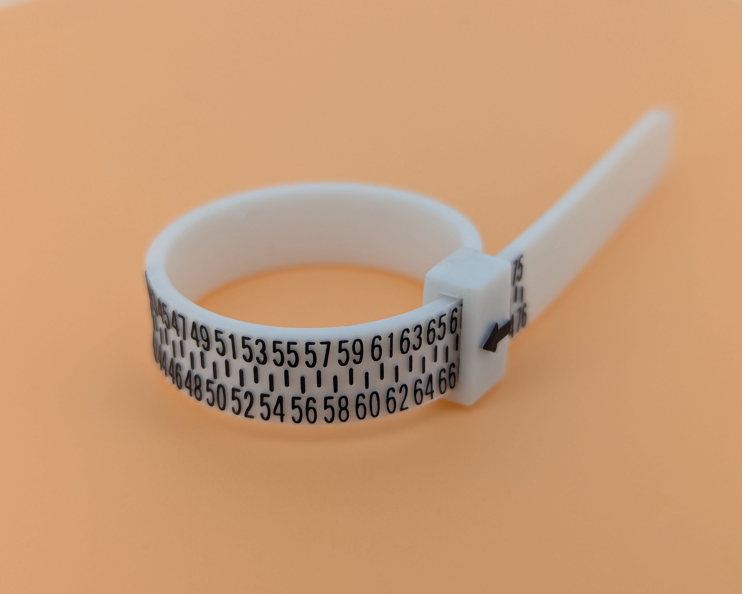 A white plastic ring sizer with black numbers and markings, placed on an orange background.