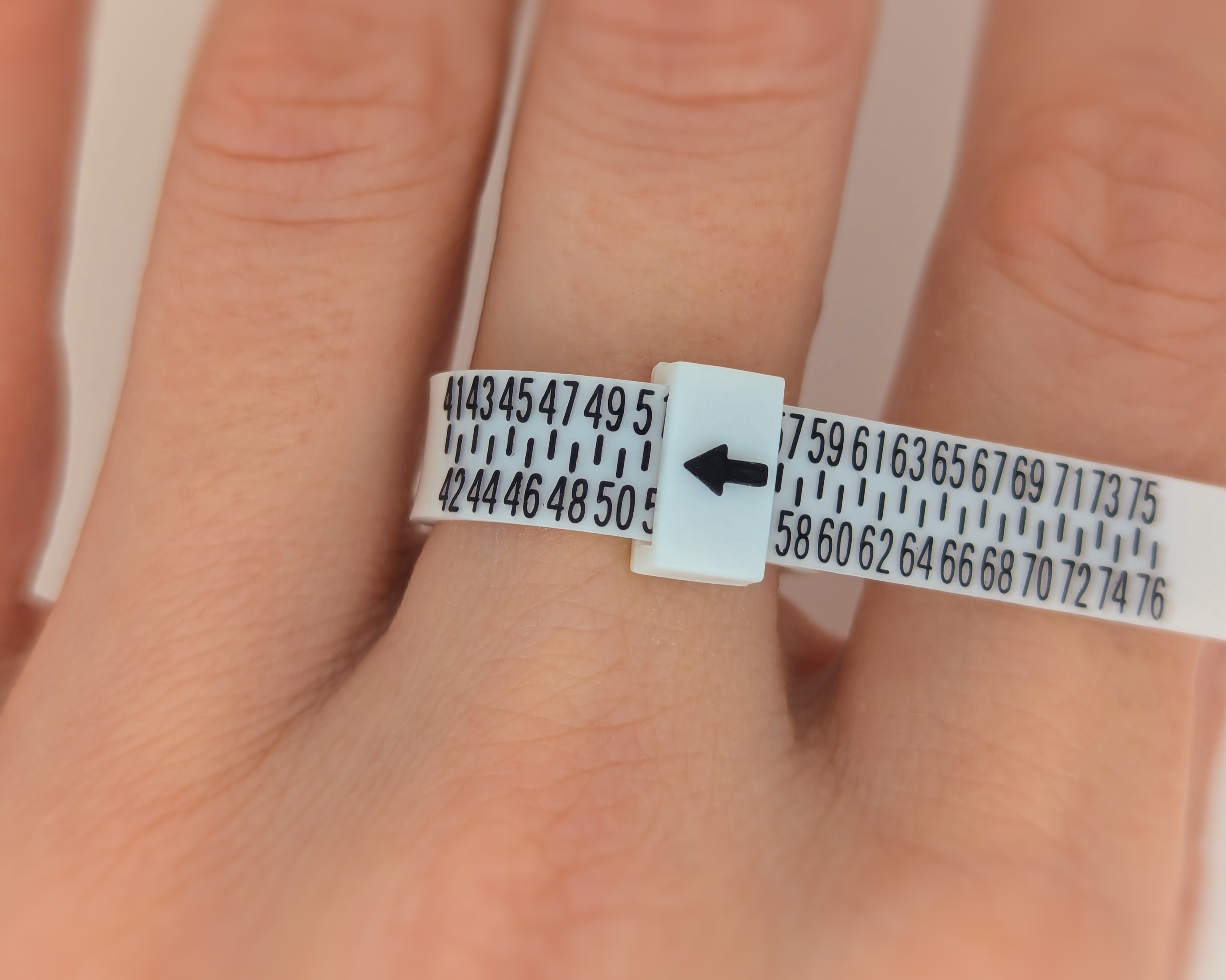 A white plastic ring sizer with black numbers and markings, worn on finger