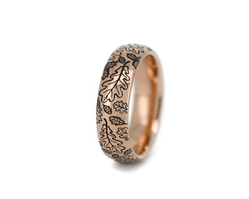 Rose gold tungsten ring with detailed oak leaf engraving on a polished band, photographed on a clean white background. Nature inspired wedding band with elegant botanical design.