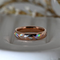 Rose-gold Botanic Glow tungsten ring with flowing holographic leaf-inspired lines, resting on a pale display surface.