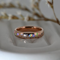 Rose-gold Lotos Glow tungsten ring with an iridescent lotus flower and leaves, resting on a pale display surface.