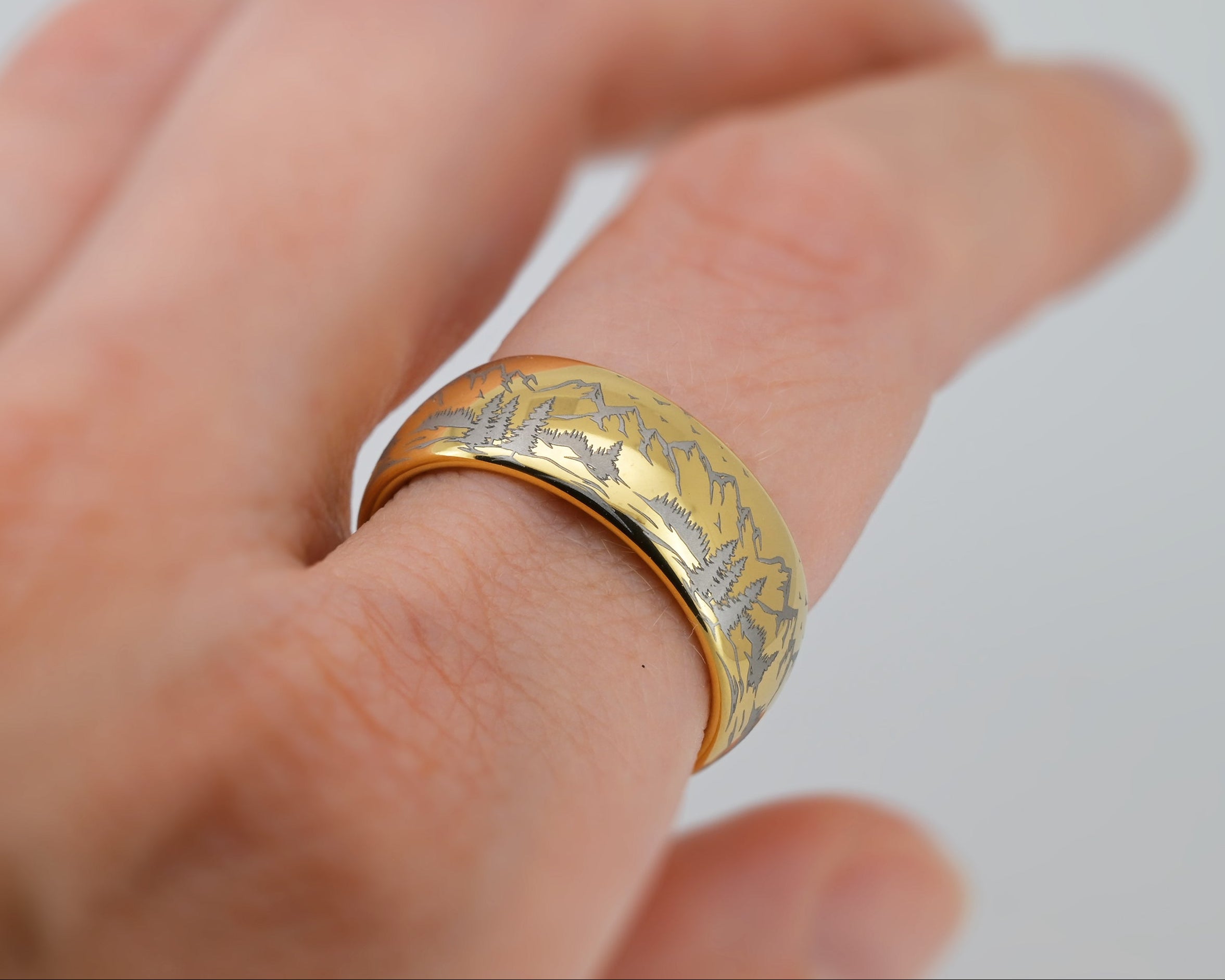Close-up of a hand wearing a gold tungsten ring with mountain engraving, showcasing outdoor-inspired design