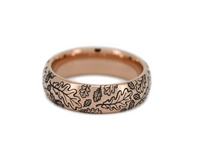 Rose gold tungsten carbide ring with black oak leaf engraving shown from front view on white background. Durable nature themed ring with minimalist woodland design.