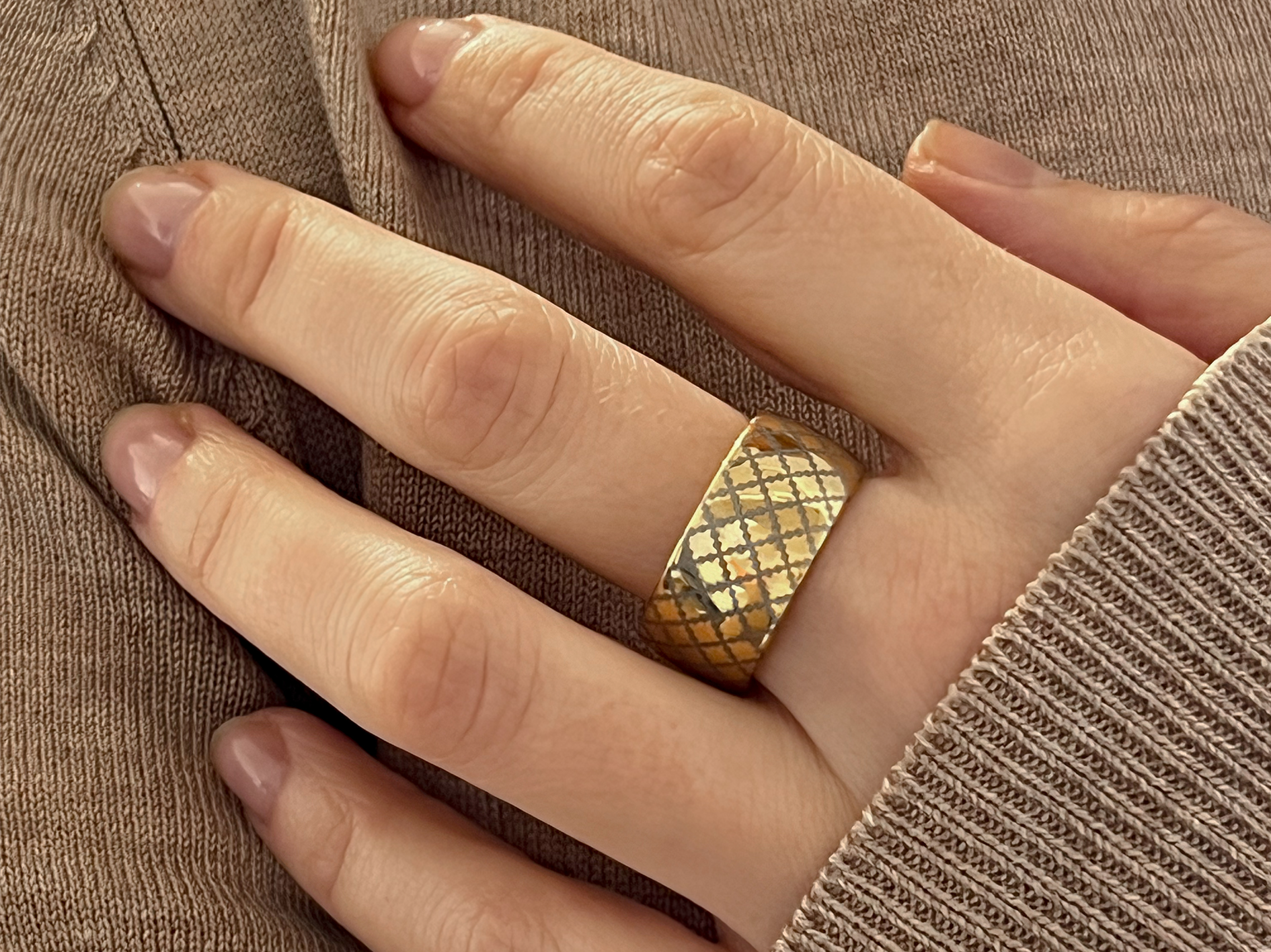 Gold tungsten ring with a quilted pattern, worn on a finger, showcasing the intricate design.