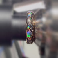 Close-up video of a rose-gold Hibiscus Glow ring on a metal holder, showing rainbow colors across hibiscus flowers and leaves.