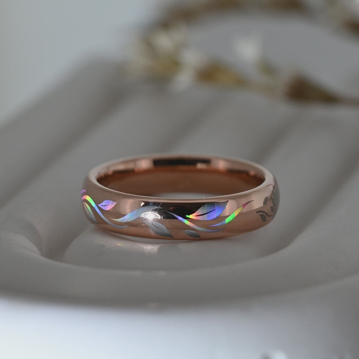 Video of a rose-gold Botanic Glow tungsten ring on a pale display surface, showing flowing holographic leaf-inspired lines.