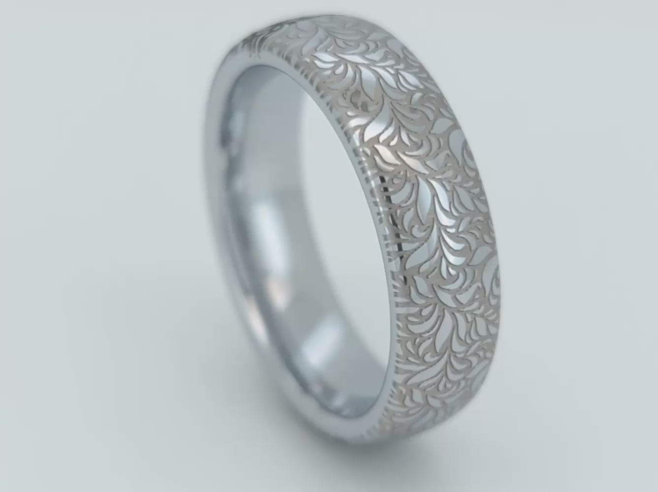 A video of elegant white gold tungsten displayed on the white background. The ring has  intricate silver floral engraving, featuring a polished shiny finish and delicate patterns. Durable and stylish, this engraved tungsten wedding or engagement band for her or him