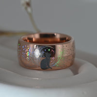 Close-up video of a rose gold holographic tungsten ring featuring a black cat, stars and celestial details with colorful rainbow reflections. Whimsical cat inspired ring with a polished finish.