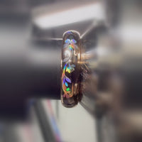 Close-up video of a rose-gold Sakura Glow ring on a metal holder, showing rainbow reflections across its sakura blossoms and leaves.