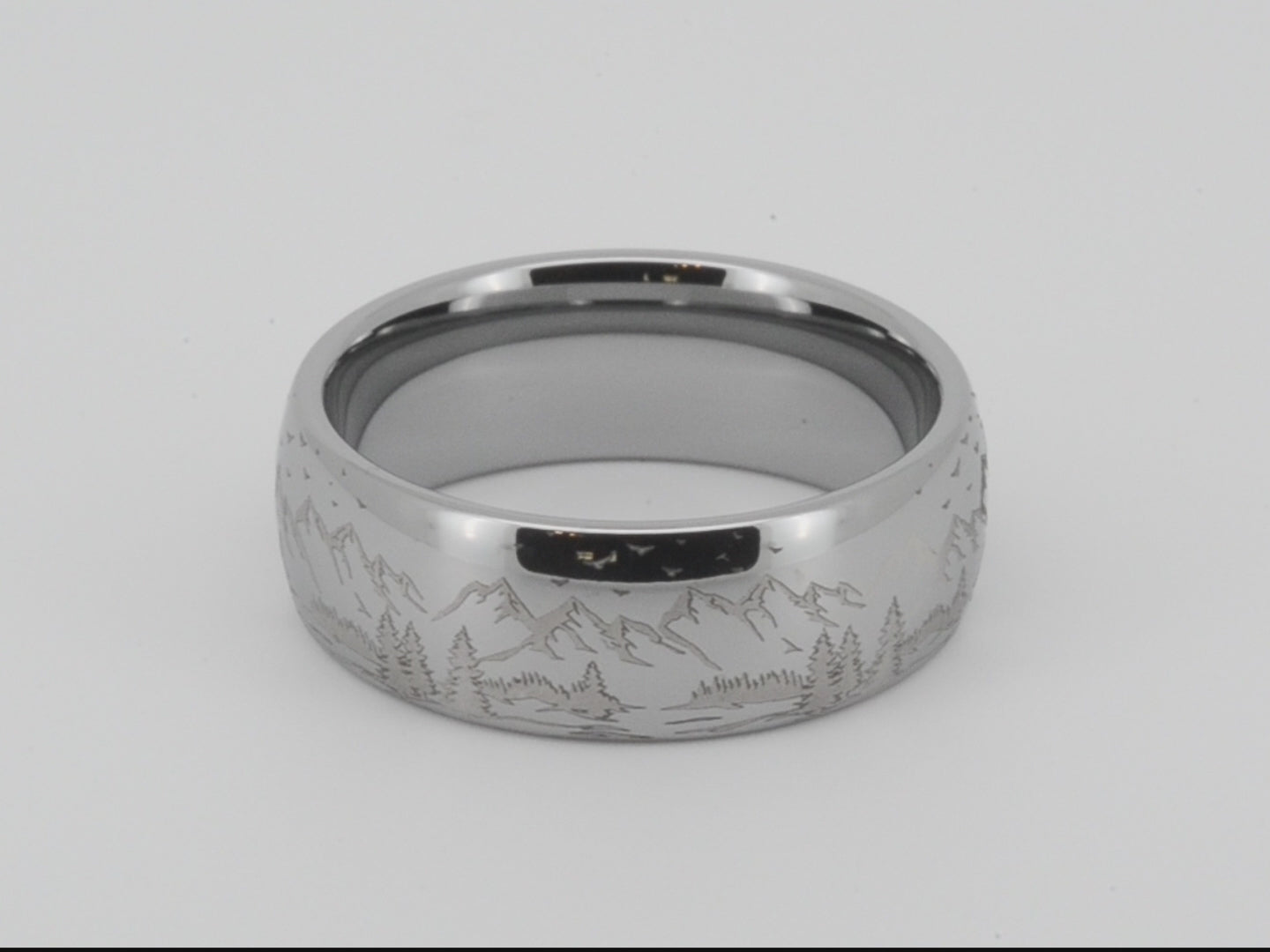 Silver tungsten ring with an engraved mountain range design, isolated on a white background.